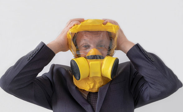 An adult man, a pensioner, in a business suit and a yellow mask-gas mask expresses the emotion of panic and fear on a white background. Horizontal orientation. Selective focus.