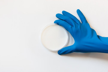 Petri dish with white liquid like milk and a blue glove that took it. Petri dish white on white, concept for medical analysis, pharmaceutical research clinics. Clinical medical research background 