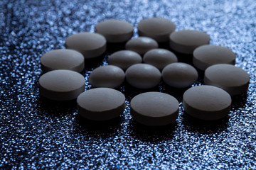 White pills, tablets capsule form a triangle in a circle on a dark shiny background