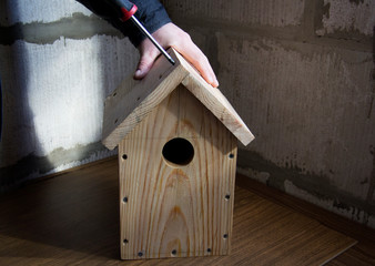 a man with a screwdriver twists a screw. He makes by hands a wooden house for birds