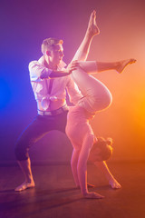 A pair of gymnasts on a blue-orange background. Girl is worth on the hands of. The man holds the girl by the waist and knee. Sport dance. Acrobats. The pair perform a trick. Keeping your balance