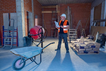 A man with a phone and building plans. Construction foreman inspects the wall of the new building. Customer at the construction site. Control of works. A man in a house under construction.