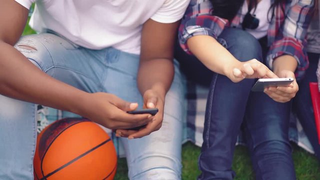 Top wiev on a group of youth sitting outdoors with smartphones in their hands. Young people checking on their social media while having a breack in between lectures.