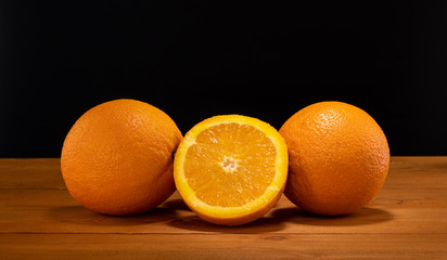 Fresh and juicy half and slice of orange fruit on a wooden table and black background.