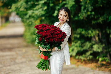 Fototapeta premium Valentine's Day 101 Birthday Gift For You. Beautiful woman with stylish makeup. Girl holding a gorgeous big bouquet of roses. Perfect sensual lips. Fashion Makeup. Woman in earrings