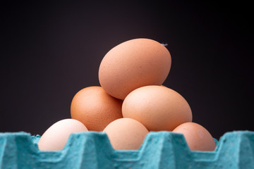 Heap of brown shaded chicken eggs in open colourful teal egg carton box in studio lighting with a dark background and part of the tray out of focus in the foreground