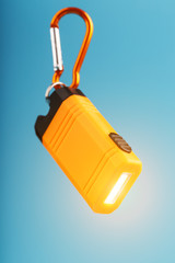 Orange led Flashlight with a carabiner on a blue background. LED lights in flight.