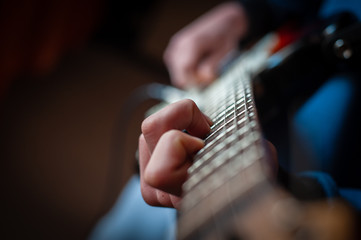 Fototapeta premium Male hands playing electric solo guitar with closeup photo. Learning musical instrument, music shop or school, blues bar or rock cafe, having fun enjoying hobby concept
