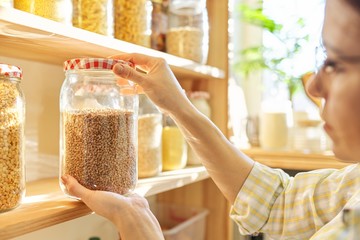 Food storage in pantry, woman holding jar of buckwheat in hand