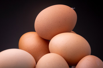 Heap of brown shaded chicken eggs in even studio light contrasted against a dark background. Macro studio food shot of shell texture and food