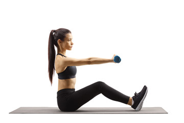 Young beautiful woman sitting on a mat and exercising with dumbbells