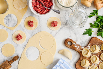 Cooking homemade meat dumplings on a marble table. Flat lay composition with ingredients and recipe. Raw ravioli with meat. Copy space. Culinary concept.