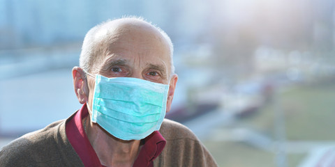 old man in protective face mask anti virus looks in camera window background