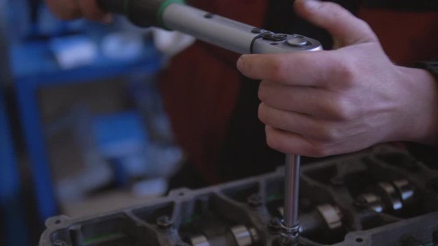 Close up of the hands of a male car mechanic screwing the nuts in the engine of a car. A man at a service station repairs a car.