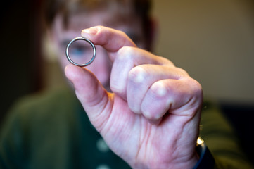 focus on hand holding a silver wedding ring with blurred male in the background