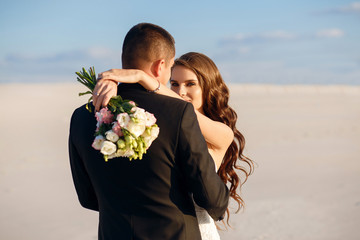 Unusual wedding photo shoot in the desert, the groom hugs the bride, sunset