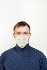 Portrait of a young man in a dark sweater on a white isolated background with copy space. He is wearing a protective mask that protects against infection, viruses, and coronavirus. His eyes are scared