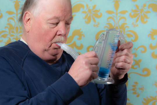 Elderly man using incentive spirometer for breath improvement.  Helpful for pneumonia or a lung condition like chronic obstructive pulmonary disease (COPD) or cystic fibrosis. 