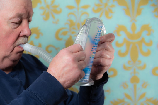 Elderly Man Using Incentive Spirometer For Breath Improvement.  Helpful For Pneumonia Or A Lung Condition Like Chronic Obstructive Pulmonary Disease (COPD) Or Cystic Fibrosis. 