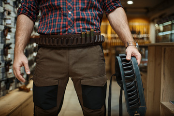 Fototapeta na wymiar Man in hunting uniform holds ammo belt in gun shop