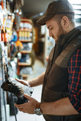 Man choosing boots for hunters in gun shop