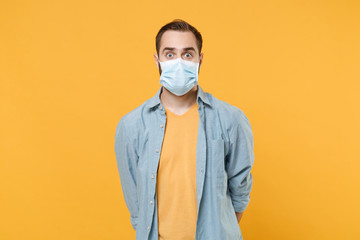Shocked young man in casual clothes, sterile face mask posing isolated on yellow background studio...