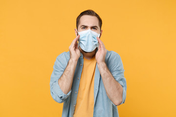 Young man in sterile face mask posing isolated on yellow wall background in studio. Epidemic...