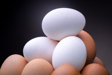 Couple of white eggs on top of several light brown chicken eggs in studio lighting contrasted against a dark grey background