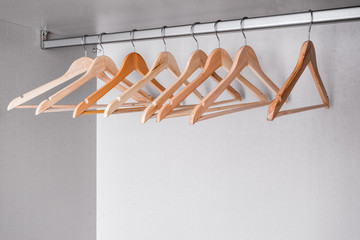 Many empty hangers made of natural, light wood of different shades hang on metal rod in wardrobe. High-quality accessories in modern furniture