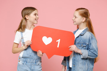Smiling little kids girls 12-13 years old in t-shirt, denim clothes isolated on pink background. Childhood lifestyle concept. Hold huge like sign from social network heart form, looking at each other.