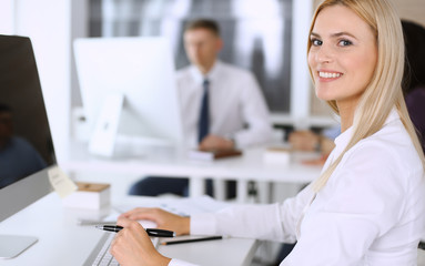 Fototapeta premium Business woman using computer at workplace in modern office. Secretary or female lawyer smiling and looks happy. Working for pleasure and success