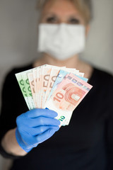 Senior woman wearing mask holds cash Euro notes in a hand in gloves. Selective focus. danger of using cash