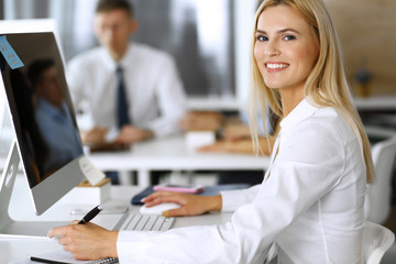 Obraz premium Business woman using computer at workplace in modern office. Secretary or female lawyer smiling and looks happy. Working for pleasure and success