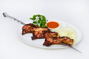 Skewers of young lamb on a rib on a white oval plate with onions and parsley, as well as tomato sauce for meat