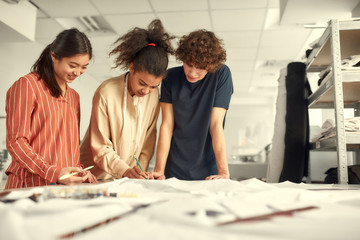 A simple place for dressmaking. Young cheerful designers working together in a studio. Group of creative millennials sharing and discussing ideas