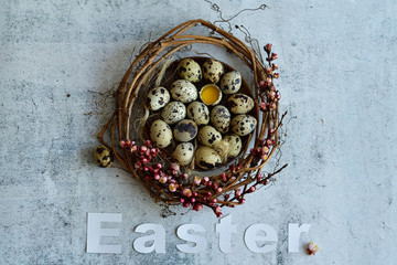 Easter wreath of grape branches, apricot flowers, quail feathers and eggs on light cement background. White letter EASTER. Copy space for greeting text, Happy Easter card, top view.