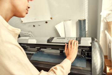 Master printing. Cropped shot of young woman controlling, monitoring printing machine while printing advertisement sticker with text or picture for a T-shirt