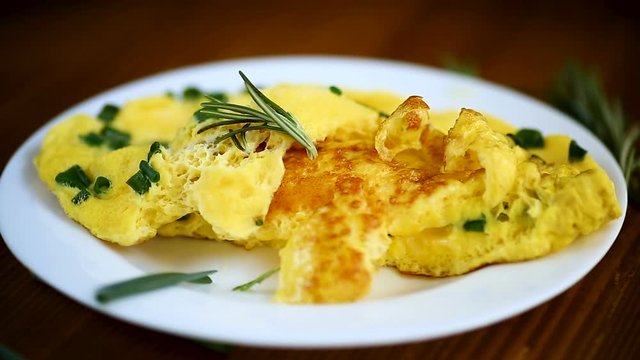 hot fried omelet with chopped green onions in a plate on a wooden table
