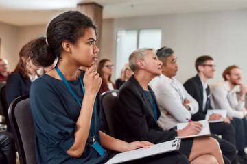 Forward-thinking. Multi-ethnic audience sitting in a row while listening to presentation at...