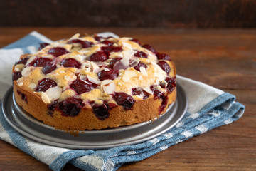 freshly baked small cherry cake with almond slivers, rustic wood and dark background with copy space, selected focus