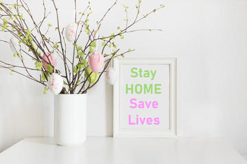 Easter concept 2020. Vase with birch tree branches with Easter eggs and frame with slogan - Stay at Home, Save Lives.