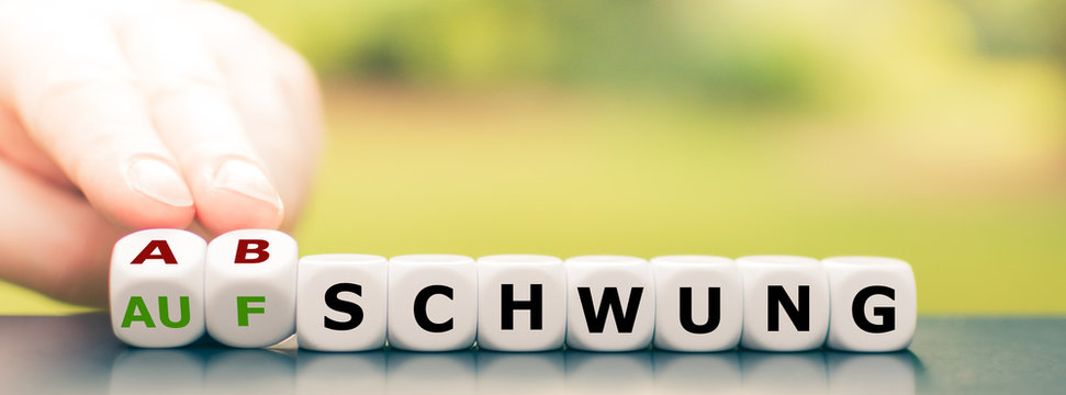 Symbol f&uuml;r wirtschaftlichen Abschwung. Hand dreht W&uuml;rfel und &auml;ndert das Wort "Aufschwung" in "Abschwung".