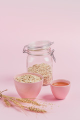 Bowl of dry oat flakes with honey and ears of wheat on light background