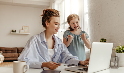 Obraz premium Joyful woman with small girl doing purchase on Internet using netbook at home.