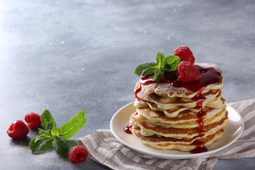 American cuisine. Breakfast. Pancakes with raspberries, sweet red topping, powdered sugar and mint in a white plate on a light grey background. Background image, copy space