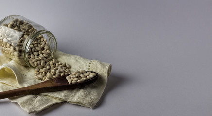  Beans in a glass jar on a cloth napkin and with a wooden spoon. White background. 