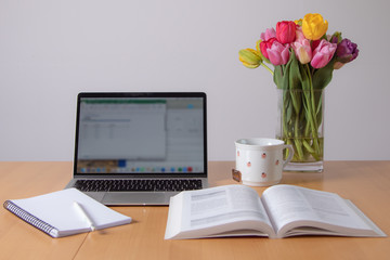 home office, laptop, book, paper, pen, flowers, tulips and a tea cup on a table at home