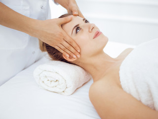 Young and blonde woman enjoying facial massage in spa salon. Beauty concept