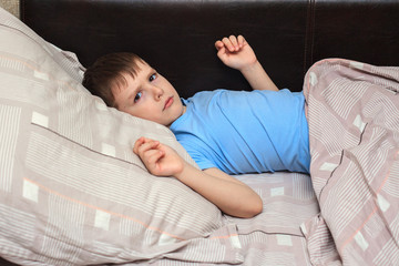 Child boy lies on the bed with a displeased face, is sick. Home quarantine. Virus. flu. Bed rest