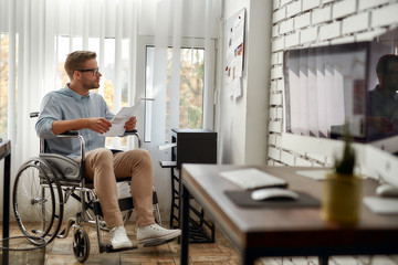 Employee working. Portrait of young male office worker in a wheelchair using printer and looking at...
